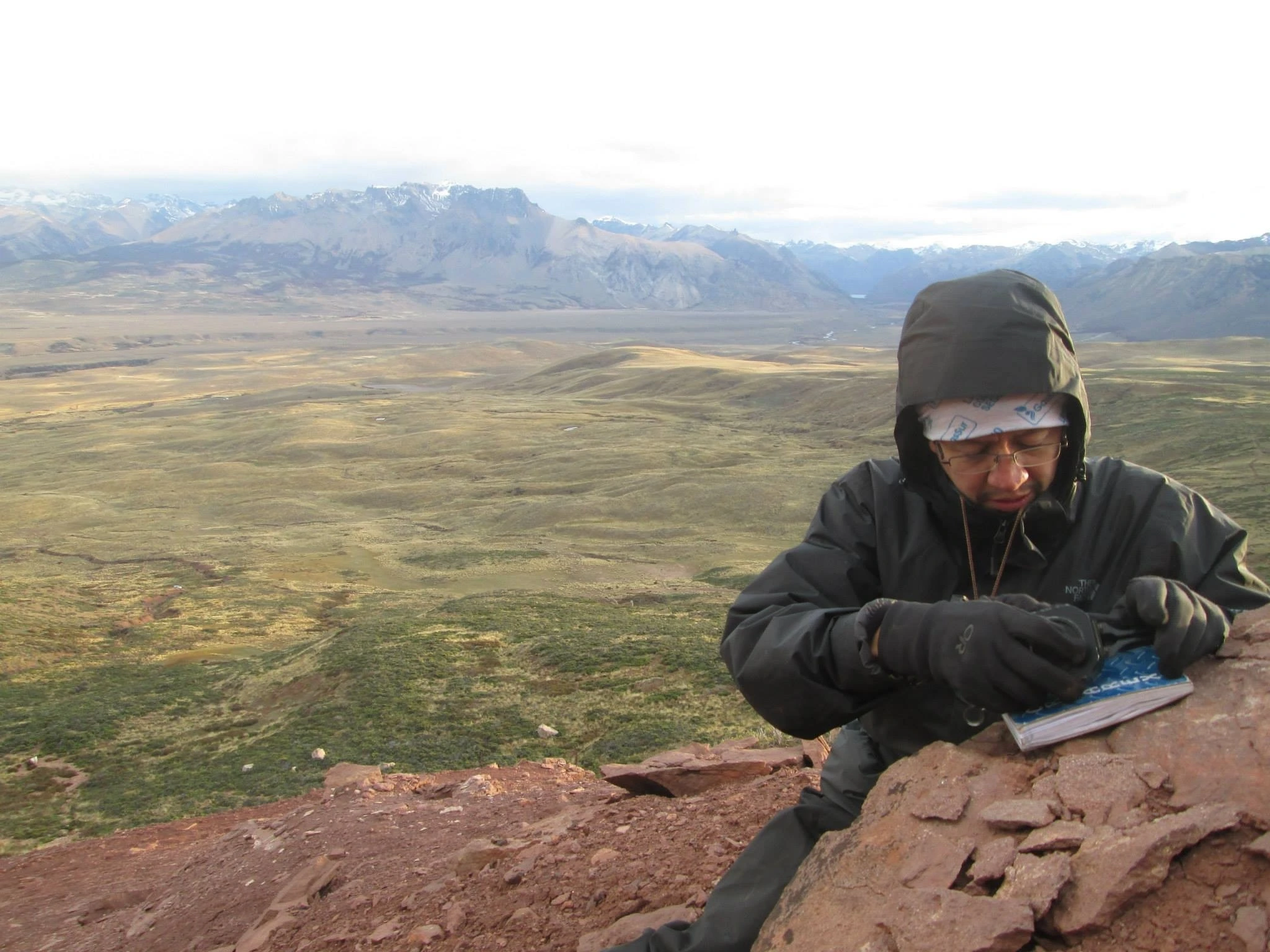 Profesional de paleontología realizando registro y levantamiento de datos en terreno rocoso montañoso.